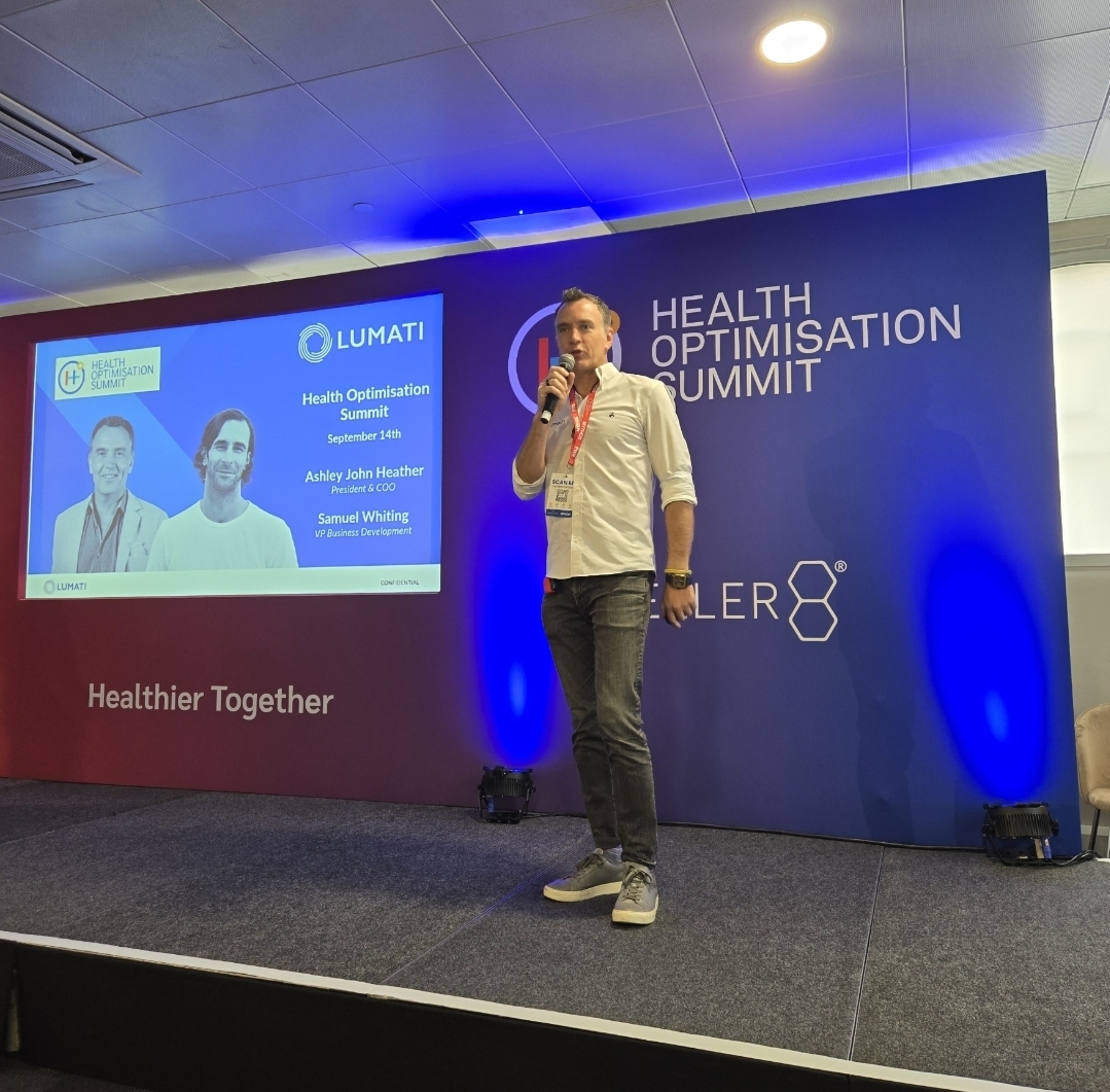 Ashley Heather speaking into a microphone on stage during a presentation at the Health Optimisation Summit.