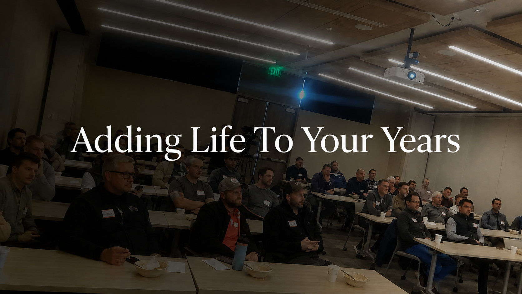 A group of professionals attending a presentation in a modern conference room, with the text “Adding Life To Your Years” displayed over the image.